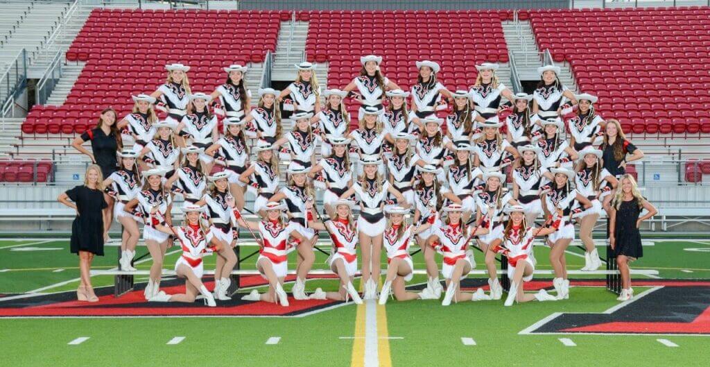 Dance team in costume, posing for group photo on the football field.