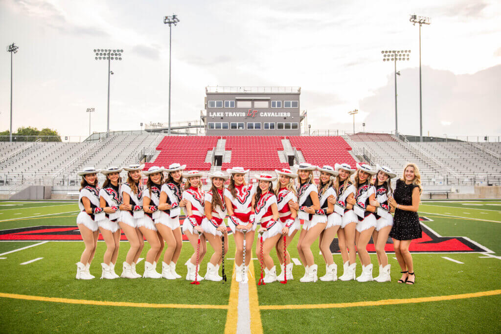 High school girls in red and white sequenced outfits with white cowgirl hats pose in a line.
