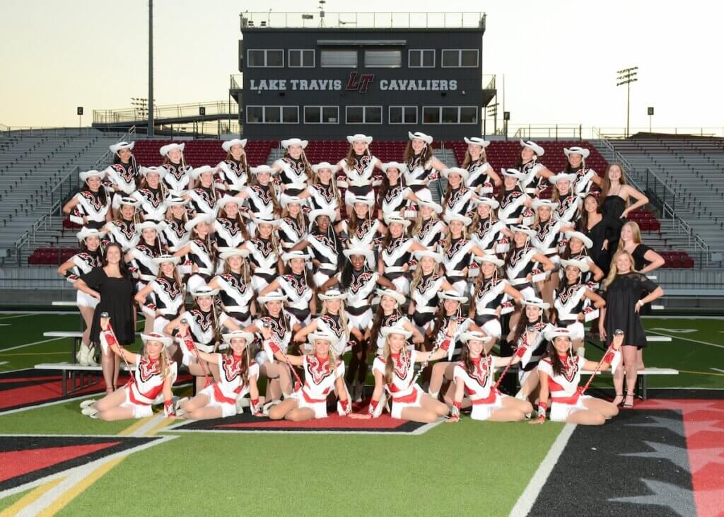 Group of high school girls in sequined outfits and cowboy hats are lined up on bleachers on the football field.
