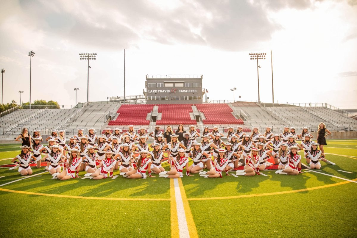 A group of cheerleaders smiles and poses together on a football field.