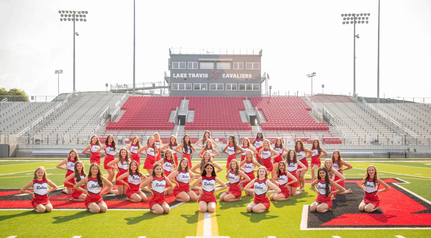 A group of young cheerleaders smiles and poses together on a football field, showcasing their vibrant uniforms.