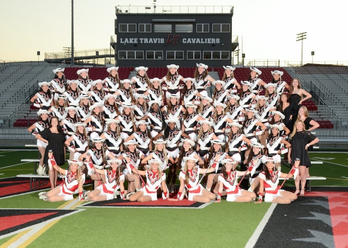 Group of high school girls in sequined outfits and cowboy hats are lined up on bleachers on the football field.