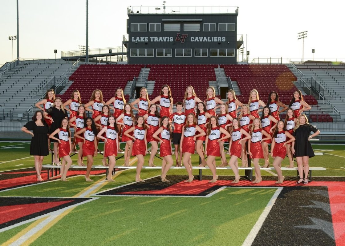 A group of high school girls in red sequined outfits, posing on the football field with left hand on hip and left foot forward.